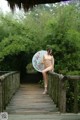 A naked woman holding an umbrella standing on a wooden bridge.