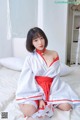 A woman in a white and red kimono sitting on a bed.