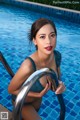 A woman in a blue bikini sitting on the edge of a swimming pool.