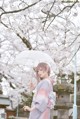 A woman in a kimono holding an umbrella in front of a tree.