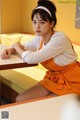 A woman sitting at a table in an orange apron.