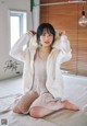 A woman sitting on a bed wearing a white jacket.