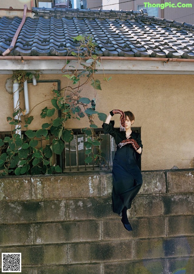 A woman in a black dress leaning against a wall.