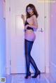 A woman in a black lingerie and high heels posing in front of a door.